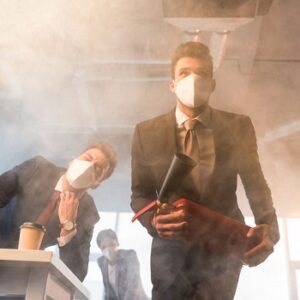 businessman in mask holding extinguisher near coworkers in office with smoke